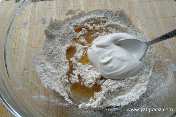 Туда же добавьте йогурт или сметану, перемешайте ложкой, а потом замесите тесто.